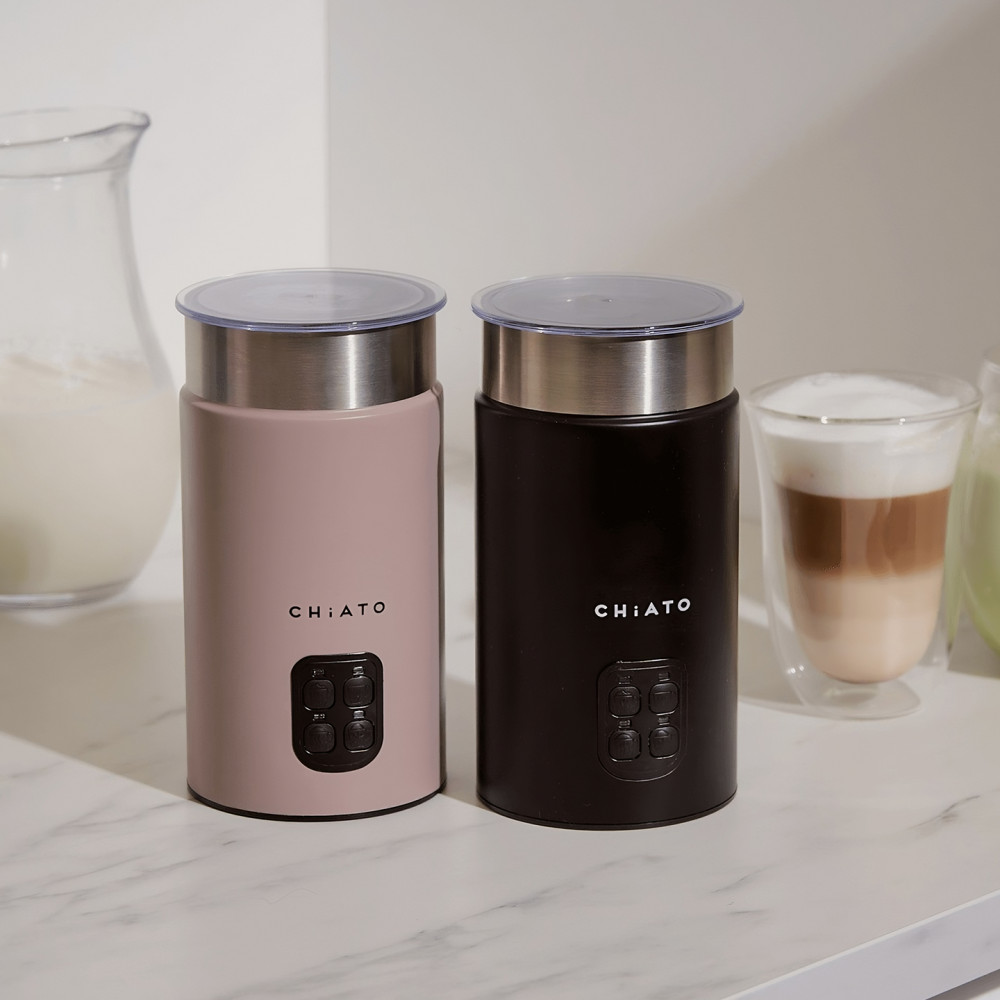 Two CHiATO milk frothers in pink and black side by side, with layered lattes and milk in the background – stylish and compact milk frothers for home use.